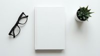 Minimalist white workspace with blank notebook, black eyeglasses and small succulent plant on clean desk surface for business planning and creative projects.