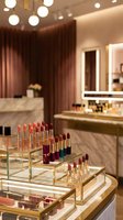 Luxury cosmetics display with colorful lipsticks in golden holders at upscale beauty store with modern interior design and warm ambient lighting.
