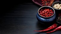 Dried red goji berries in traditional Chinese ceramic bowl on dark wooden background with chili peppers, healthy superfood concept for wellness.