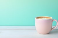 Pink coffee cup with creamy latte on white wooden table against mint green wall background, minimalist composition for cafe menu or social media content.
