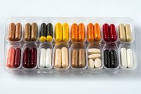 Colorful assortment of medical supplements and vitamin pills in transparent plastic organizer compartments arranged in neat rows showing variety of capsules and tablets.