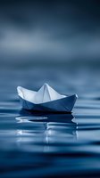 White paper boat floating on calm blue water surface with soft reflections and dreamy bokeh background for creative projects and nautical themes.