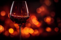 Glass of red wine against warm bokeh background with orange and red glowing lights creating romantic atmosphere for restaurant menu or wine tasting event.