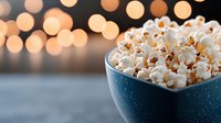 Fresh popcorn in blue speckled bowl against blurred warm bokeh lights background, creating cozy movie night atmosphere. Perfect for entertainment concepts.