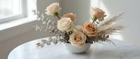 Elegant floral arrangement with cream and peach roses, eucalyptus and pampas grass in white ceramic vase on marble table for home decor and styling.