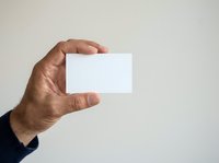 Male hand holding blank white business card against neutral background, suitable for corporate branding, identity design, and professional marketing materials.