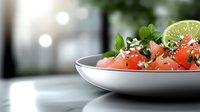 Fresh watermelon salad with mint leaves and lime garnish served in white bowl on kitchen counter for healthy summer dining and refreshing meal preparation.