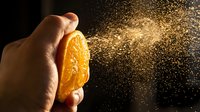 Hand squeezing fresh orange with juice spray particles bursting outward against dark background, capturing dynamic citrus freshness and natural vitamin C content for beverage and health concepts.