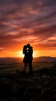Silhouetted couple kissing on rocky hilltop at golden sunset with dramatic orange and purple sky, countryside landscape below, romantic outdoor moment for love and relationship content.