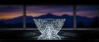Elegant crystal glass bowl with intricate cut patterns on dark surface against mountain sunset backdrop for luxury dining and home decor concepts.