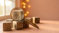 Financial analysis concept with magnifying glass examining percentage symbols on wooden blocks representing interest rates and investment research.