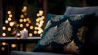 Luxurious dark teal velvet cushion with metallic gold feather pattern against blurred holiday lights background creates cozy home atmosphere.