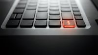 Close-up of laptop keyboard with glowing red enter key highlighting cybersecurity breach, hacking attack or system alert for technology concepts.