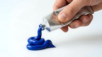 Hand squeezing blue acrylic paint from tube onto white surface for art projects, crafts, and creative painting activities on isolated background.