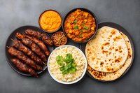 Traditional Indian cuisine with grilled seekh kebabs, butter chicken curry, basmati rice, naan bread and mango chutney served on dark background.