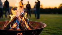 Crackling campfire flames dance in metal fire pit during golden hour sunset with silhouetted people gathering in background for outdoor evening social activity.