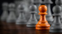 Orange wooden pawn stands out among gray chess pieces on board, symbolizing leadership, strategy, uniqueness, and competitive advantage in business and games.