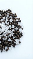 Black peppercorns and coarse sea salt crystals scattered on white background for culinary seasoning and cooking applications.