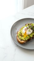 Avocado toast with poached egg on gray plate, topped with microgreens and red pepper flakes on marble surface. Perfect for brunch, healthy eating, and food photography.