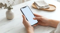 Female hands holding smartphone with blank white screen mockup on marble table with eucalyptus plant and ballet flats for app presentation.