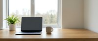 Modern minimalist home office workspace with laptop computer and coffee mug on wooden desk near bright window for remote work and productivity.