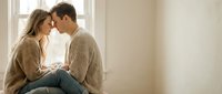 Young Caucasian couple sharing intimate moment by window in cozy home setting. Romantic lifestyle photography for relationship and love concepts.