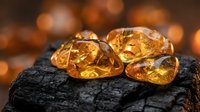 Amber gemstones with ancient insect inclusions on dark volcanic rock surface with warm golden bokeh background for jewelry design.