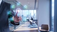 Businessman touching glowing lightbulb icon with digital innovation symbols in modern office environment representing creative business solutions and technology.