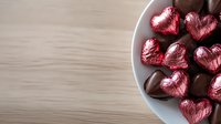 Heart shaped pink foil wrapped chocolate candies in white ceramic plate on wooden table background with copy space for Valentine's Day message.