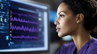 African American female medical professional in purple scrubs viewing patient vital signs on monitor display, side profile portrait showing focused concentration.