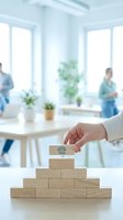 Hand placing wooden block with team icon on pyramid stack, representing business growth, leadership, and organizational structure in modern office.