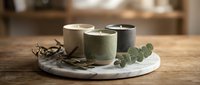 Scented candles in neutral tones arranged on marble tray with dried botanicals and eucalyptus for home decor and wellness styling.