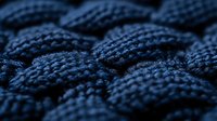 Close-up macro shot of dark blue woven textile pattern showing detailed fabric texture and intricate braided or knitted material structure in soft lighting.
