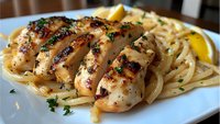 Grilled chicken breast slices with creamy pasta and herbs on white plate. Restaurant quality meal ready for menu design and culinary marketing materials.