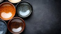 Rustic ceramic bowls with textured glazes in earthy tones arranged on dark stone background, minimalist composition with copy space for food photography.