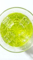 Bright green cocktail with ice cubes in a crystal glass, top view on white background. Refreshing summer drink concept for menu and bar design.