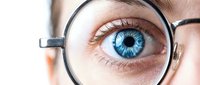 Close-up of blue eye magnified through eyeglasses lens showing detailed iris and pupil for vision care and optical health concepts.