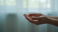 Open cupped hands in gentle receiving gesture against soft blurred background suggesting hope, prayer, support and spiritual connection in peaceful moment.