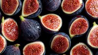 Fresh ripe purple figs cut in half showing bright pink flesh and seeds arranged in rows on dark background, organic healthy Mediterranean fruit.