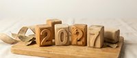 Wooden blocks with numbers 2027 arranged on a cutting board with dried leaves and burlap ribbon, celebrating the upcoming new year.