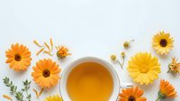 Herbal tea cup surrounded by fresh yellow and orange gerbera daisies and chamomile flowers on white background for wellness and natural beverage design.