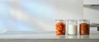Three glass jars on kitchen counter containing fermented foods and milk, showcasing homemade preservation and healthy probiotic ingredients for cooking.