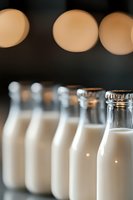 Fresh milk bottles lined up in row with soft bokeh lights background, selective focus on glass container showing creamy white dairy beverage.
