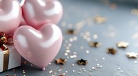 Pink heart-shaped balloons with golden gift box and star confetti on gray surface for romantic celebrations and love-themed events.