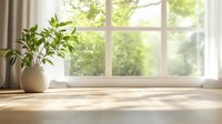 Sunlit windowsill with white ceramic pot and green plant casting soft shadows on wooden surface. Natural morning light streams through window creating peaceful home atmosphere.