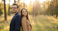 Young professional couple standing back to back in autumn forest during golden hour sunset wearing business casual attire and glasses for lifestyle photography.