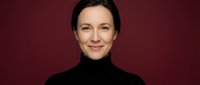 Professional middle-aged Caucasian businesswoman in black turtleneck smiling confidently against burgundy background for corporate presentations.