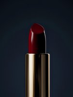 Deep burgundy red lipstick in luxurious gold metallic case against dark background, dramatic studio lighting highlighting glossy texture and elegant design.