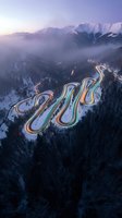Aerial view of a winding mountain road with colorful lane markings cutting through snow-covered forest and misty peaks at dawn, suitable for travel and landscape design projects.