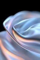 Smooth flowing curves of silky fabric in light blue and peach tones against dark background create elegant abstract composition with soft lighting effects.